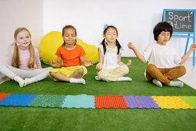 Kinder auf einem Wiesenteppich in Meditationshaltung